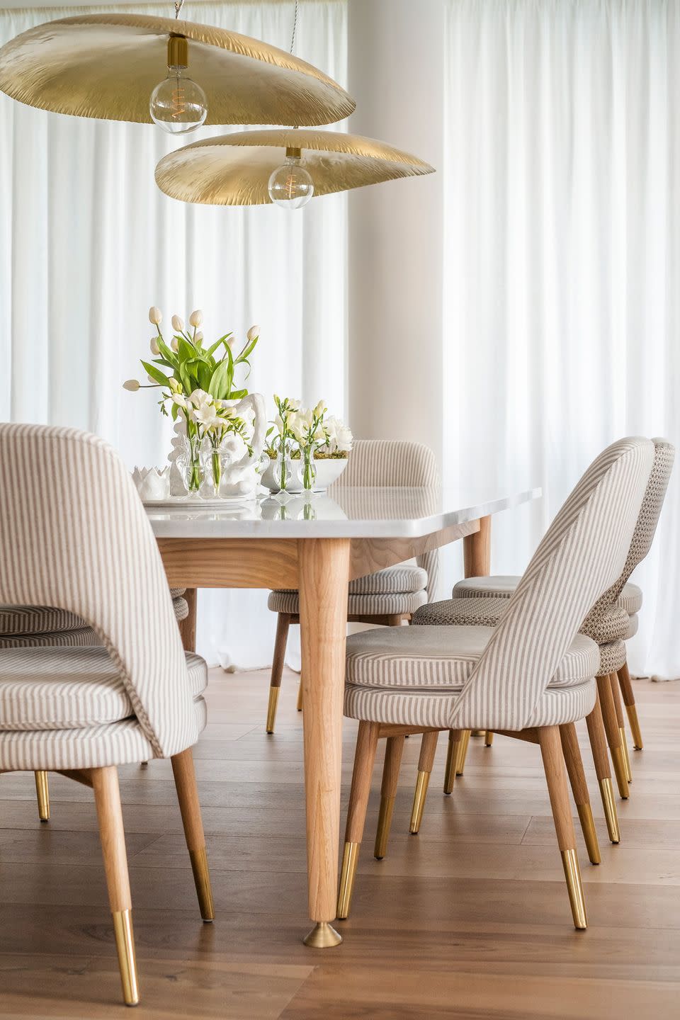 comedor con mesa de mármol, sillas tapizadas a rayas y lámparas suspendidas de metal dorado