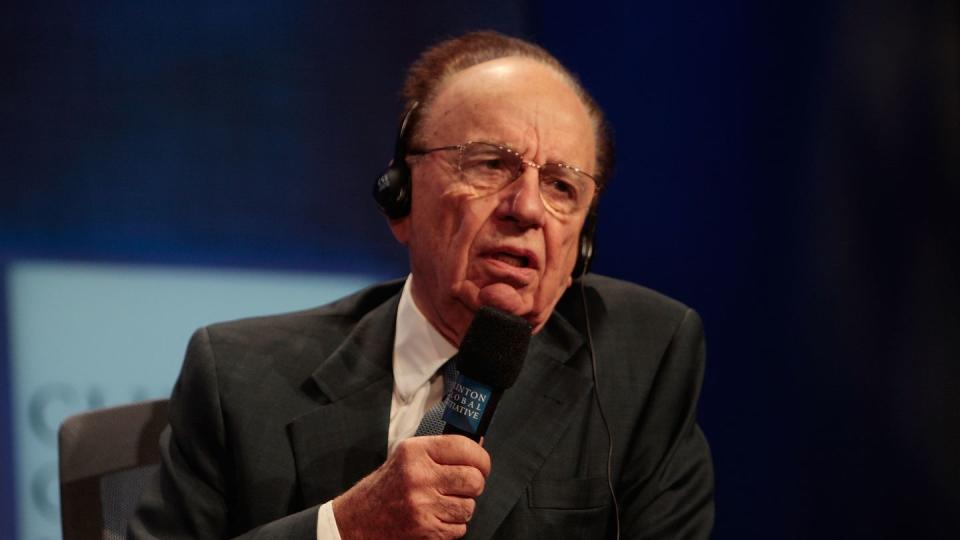 rupert murdoch wearing headphones and speaking into a microphone while sitting in a chair