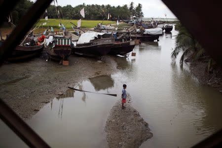 A boy stands on a sandbank near Rohingya fishermen working on their boats at Thae Chaung refugee camp outside Sittwe November 7, 2014. REUTERS/Minzayar/Files