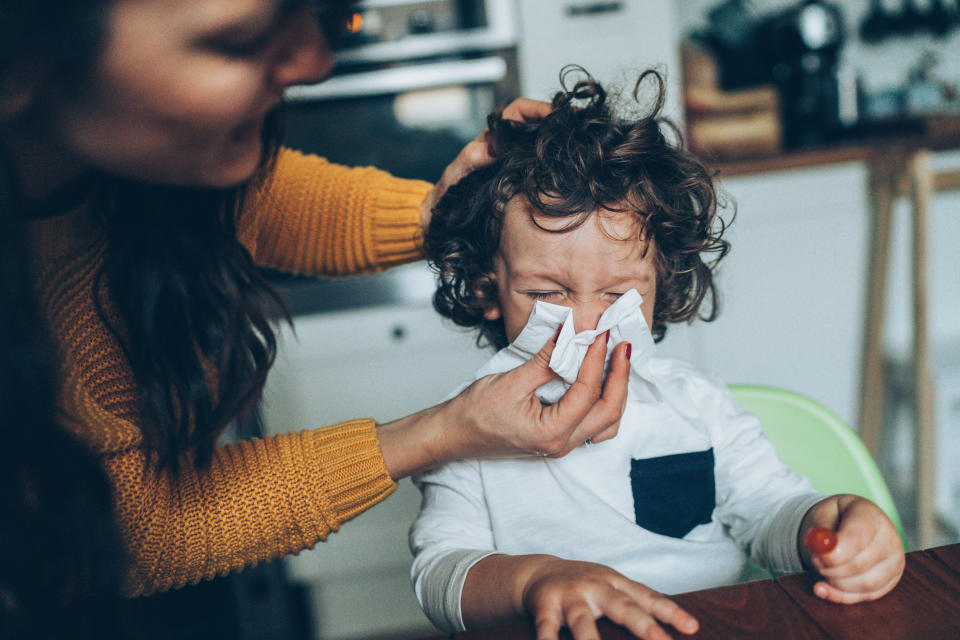 A woman helps a toddler blow his nose.