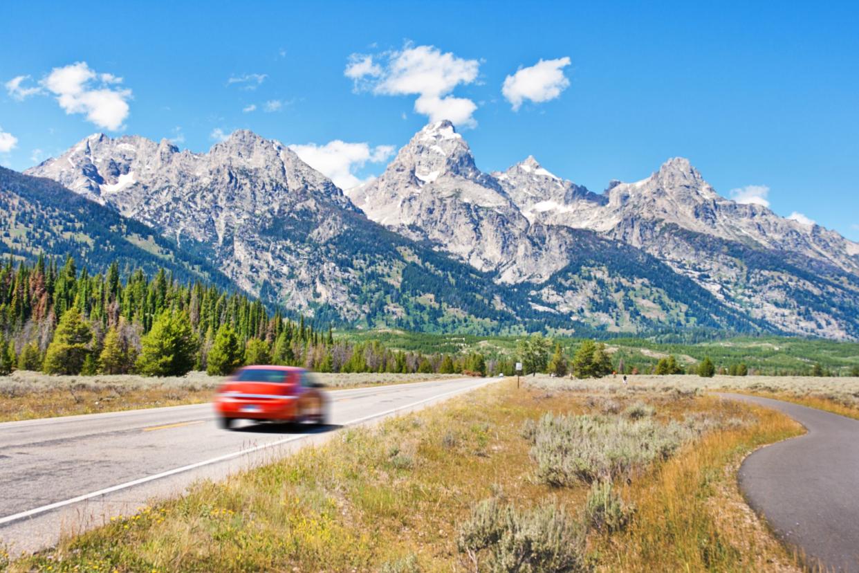 Subject: Driving vacationing in the Grand Teton National Park, a automobile driving on the highway of the Grand Teton, a popular vacation destination of the American Rockies.