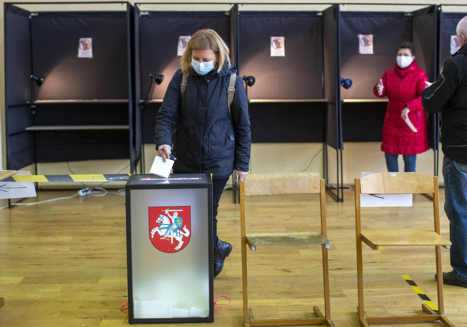 A woman, wearing face masks to protect against coronavirus, casts her ballot at a polling station during the second round of a parliamentary election in Vilnius, Lithuania, Sunday, Oct. 25, 2020. Polls opened Sunday for the run-off of national election in Lithuania, where the vote is expected to bring about a change of government following the first round, held on Oct. 11, which gave the three opposition, center-right parties a combined lead. (AP Photo/Mindaugas Kulbis)