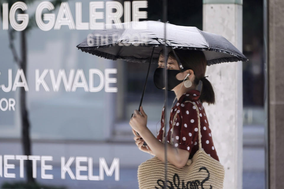 A woman wearing a protective mask to help curb the spread of the new coronavirus is reflected on a mirror window of a shop Wednesday, Aug. 12, 2020, in Tokyo. Hot weather Wednesday has set with temperatures rising up over 34 degrees Celsius (93.2 degrees Fahrenheit) in Tokyo, according to the Japan Meteorological Agency. (AP Photo/Eugene Hoshiko)