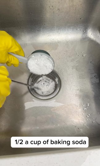 Hand in glove pouring baking soda into a cup in a sink, with caption "1/2 a cup of baking soda."