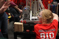 A member of the Smithtown robotics team is making some last minute adjustment to a gearbox while listening to her coach's advice for their next match.