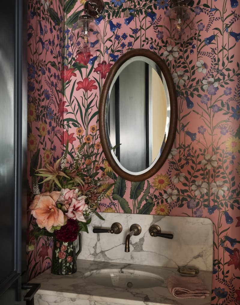 A bathroom decorated with floral wallpaper and a circular mirror