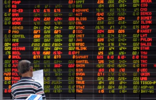 A Thai investor reads a document in front of an electronic shares price display at the stock exchange in Bangkok, 2009. Asian markets fell and the euro was at a near two-year low against the dollar amid Europe's deepening debt woes, while disappointing US data and Chinese manufacturing numbers also weighed