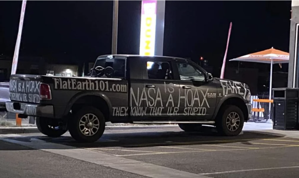 Pickup truck with messages like &quot;FlatEarth101 dot com&quot; and &quot;NASA is a hoax they know that UR stupid&quot; written all over it