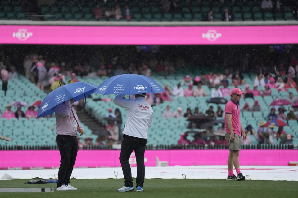 Two match officials use umbrellas as they inspect the pitch during a rain delay on the third day of the cricket test match between Australia and South Africa at the Sydney Cricket Ground in Sydney, Friday, Jan. 6, 2023. (AP Photo/Rick Rycroft)