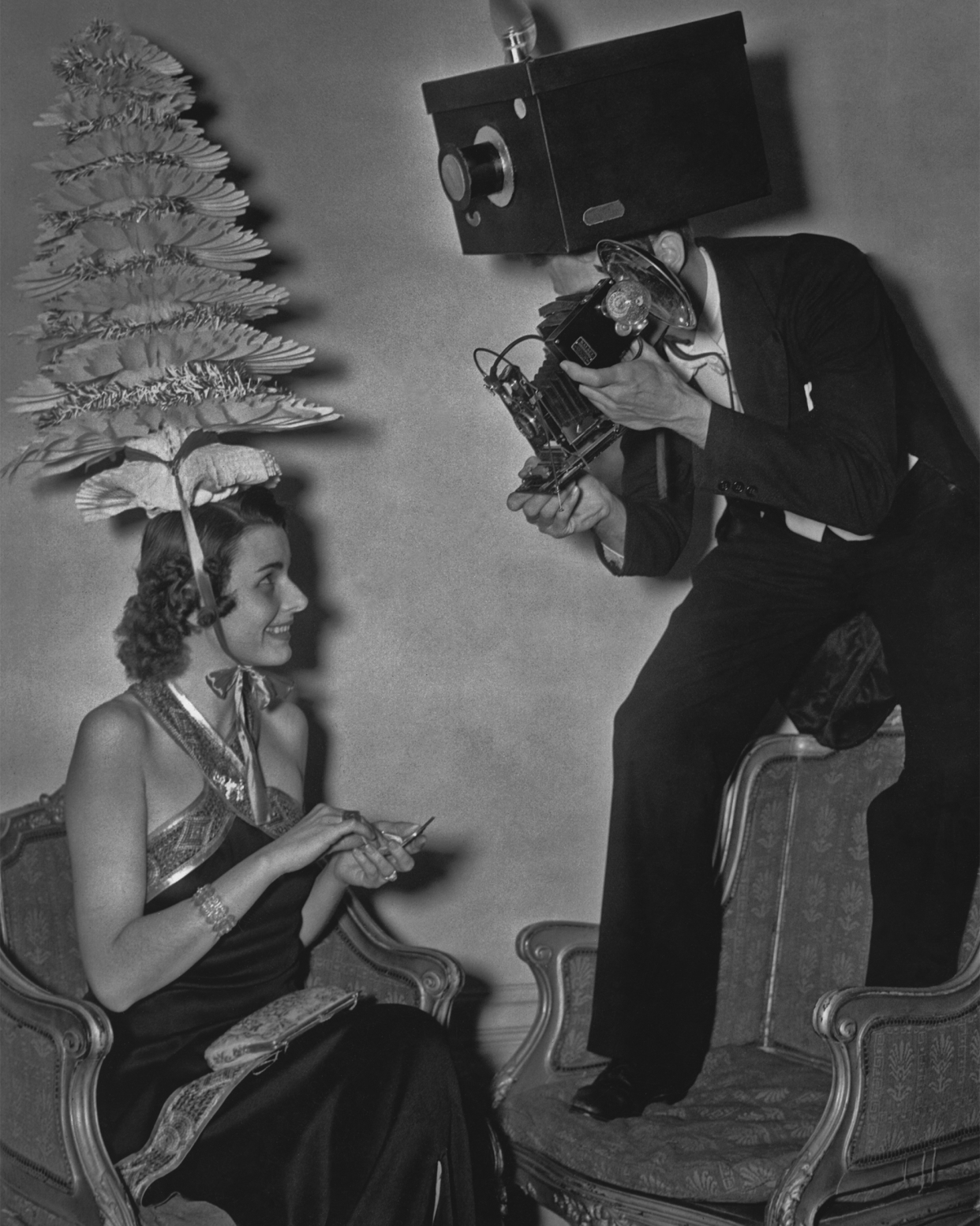 A man wearing a model of a box camera on his head takes a photograph of Mrs George Peterson Jnr