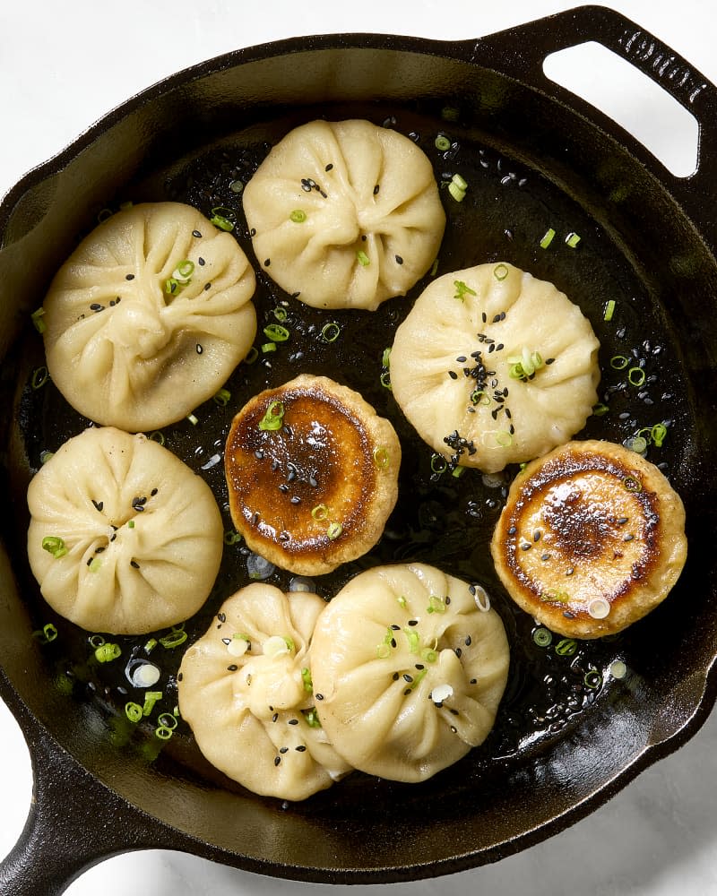 A cast iron skillet with a cooked batch of sheng jian bao (pan fried pork buns) in it with two flipped up showing the seared bottoms.