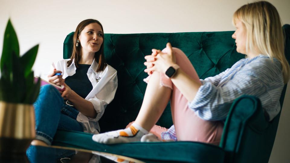 Safe space to deal with menopause issues and aging problems: Middle-aged female psychotherapist and mature female patient sitting on green couch communicating while looking at each other