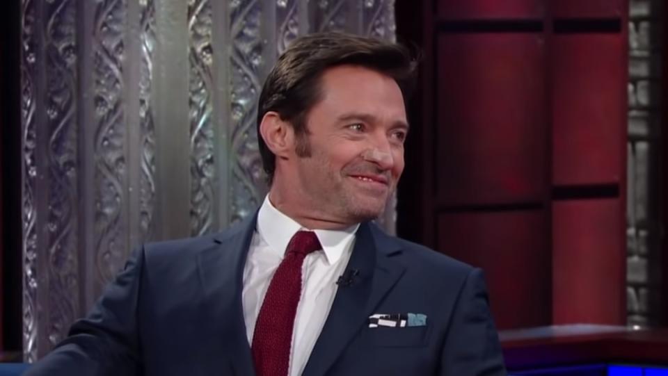 a photo of actor hugh jackman wearing a blue suit, red tie, and white shirt looking off to the right