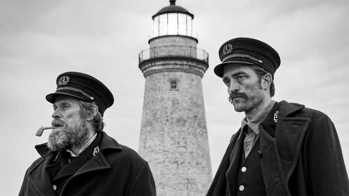 Willem Dafoe and Robert Pattinson in character with a lighthouse in the background in The Lighthouse.