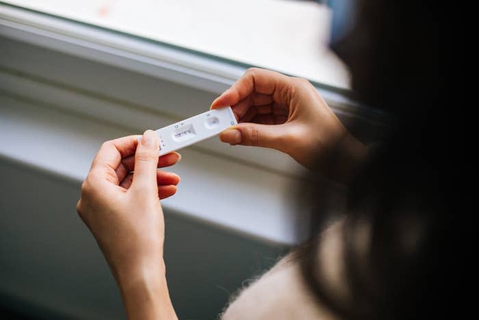 Two hands holding a pregnancy test kit inside a room next to a window