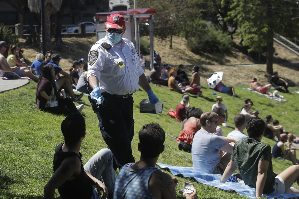 San Francisco Police Auxiliary Law Enforcement Response Team (ALERT) volunteer David Flynn offers face masks to help prevent the spread of the coronavirus at Dolores Park in San Francisco, Sunday, May 24, 2020. (AP Photo/Jeff Chiu)