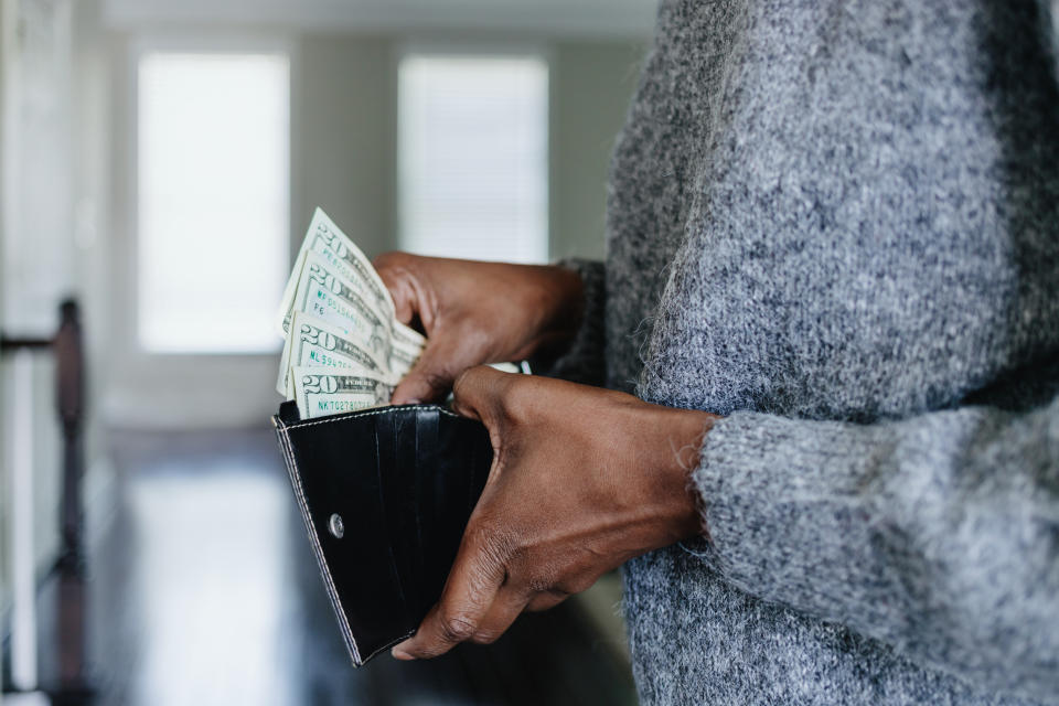 Person holding wallet with several dollar bills visible