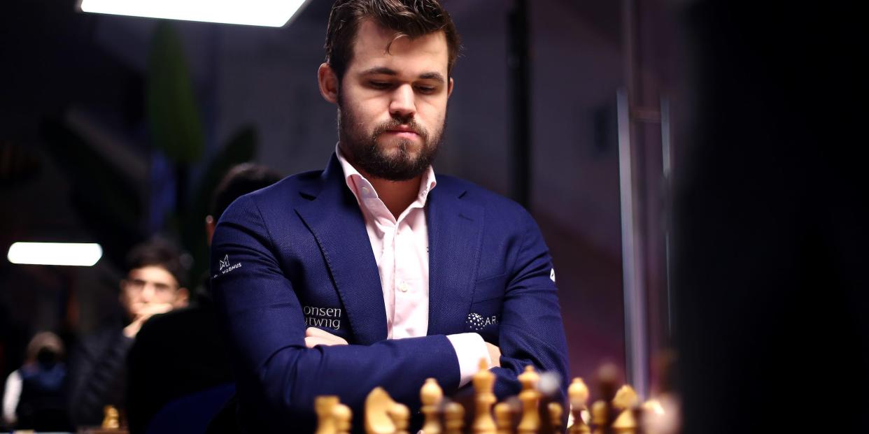 Magnus Carlsen looks down at a chessboard with his arms crossed