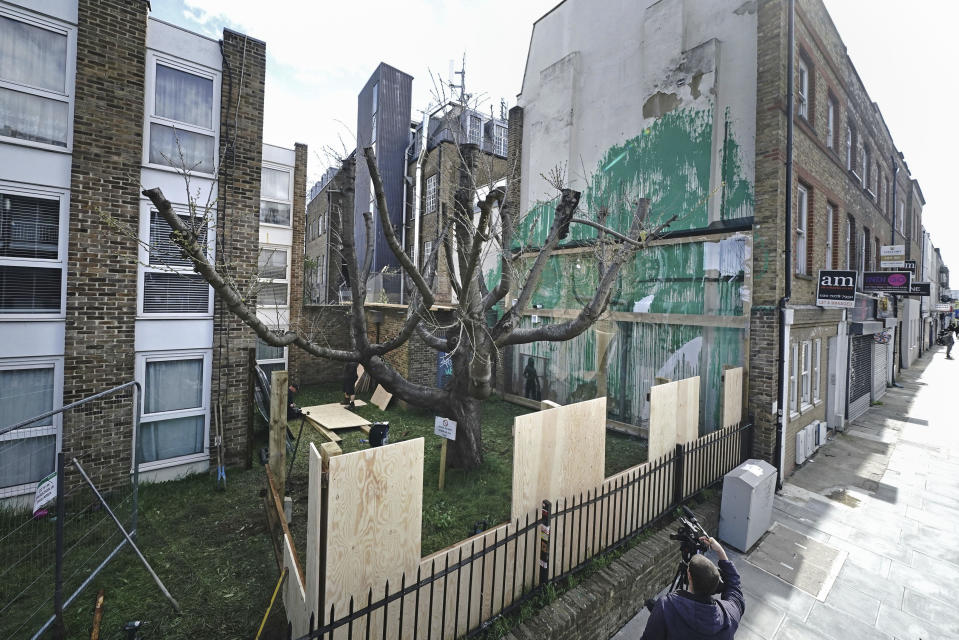 Boarding is put up next to the Banksy artwork on the side of a residential building in Hornsey Road, north London, Wednesday March 27, 2024 which has been covered in perspex sheeting for protection. An environmentally themed mural in London by street artist Banksy has been encased in plastic and surrounded by fencing after an apparent act of vandalism. (Aaron Chown/PA via AP)