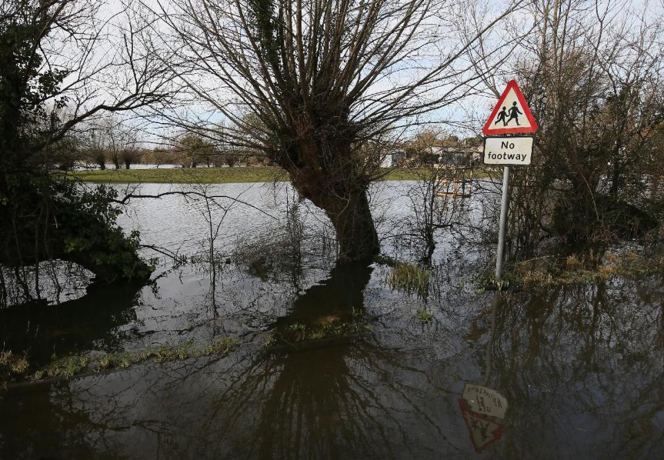 In this photo taken Sunday Feb. 2, 2014, A road sign telling drivers to take care of pedestrians is seen on the flooded road between Langport and Muchelney in Somerset, England, the village has been cut off by road since Jan. 1 this year. Here on the Somerset Levels _ a flat, marshy region of farmland dotted with villages and scored by rivers and ditches _ it's often wet. But not this wet. Thousands of acres of this corner of southwest England have been under water for weeks, some villages have been cut off for more than a month, and local people forced to take boats to get to school, work and shops are frustrated and angry. Some blame government budget cuts and environmental bureaucracy. Others point to climate change. Even plump, endangered water voles are the target of ire. (AP Photo/Alastair Grant)