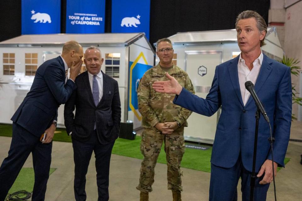 After touring tiny homes at Cal Expo, Gov. Gavin Newsom answers questions from the media in March after announcing that the state will have 1,200 of the homes built and delivered throughout California to help house the homeless population. Assemblyman Kevin McCarty, D-Sacramento, whispers to Sacramento Mayor Darrell Steinberg at left, as California National Guard Maj. Gen. Matt Beevers listens. Renée C. Byer/rbyer@sacbee.com