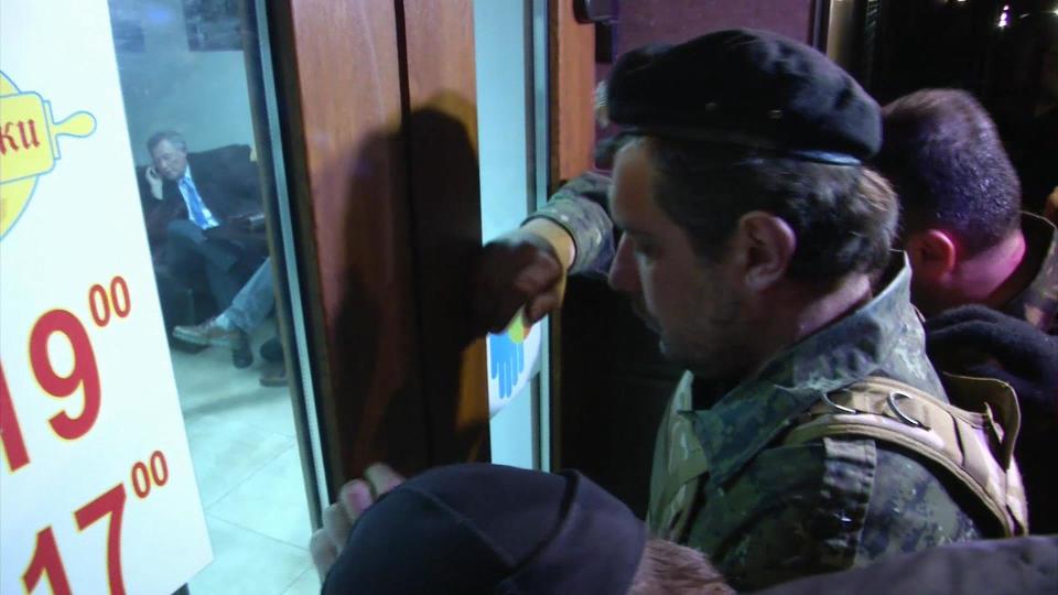 This image taken from AP video shows a group of unidentified men in military fatigues outside a cafe in Simferopol, Ukraine who appear to be stopping UN Special Envoy to Ukraine, Robert Serry from leaving as he makes a call on his mobile phone inside, Wednesday, March 5, 2014. The special U.N. envoy who is visiting Crimea was threatened by 10 to 15 armed men on Wednesday and ordered to leave the region, where Ukraine and Russia are locked in a tense standoff, U.N. officials said. Later, an Associated Press reporter found Robert Serry in the business class lounge of the Simferopol airport on Wednesday evening. "I'm safe. My visit was interrupted for reasons that I cannot understand," the Dutch diplomat said in a statement to AP. He said nothing more. (AP Photo/AP video)