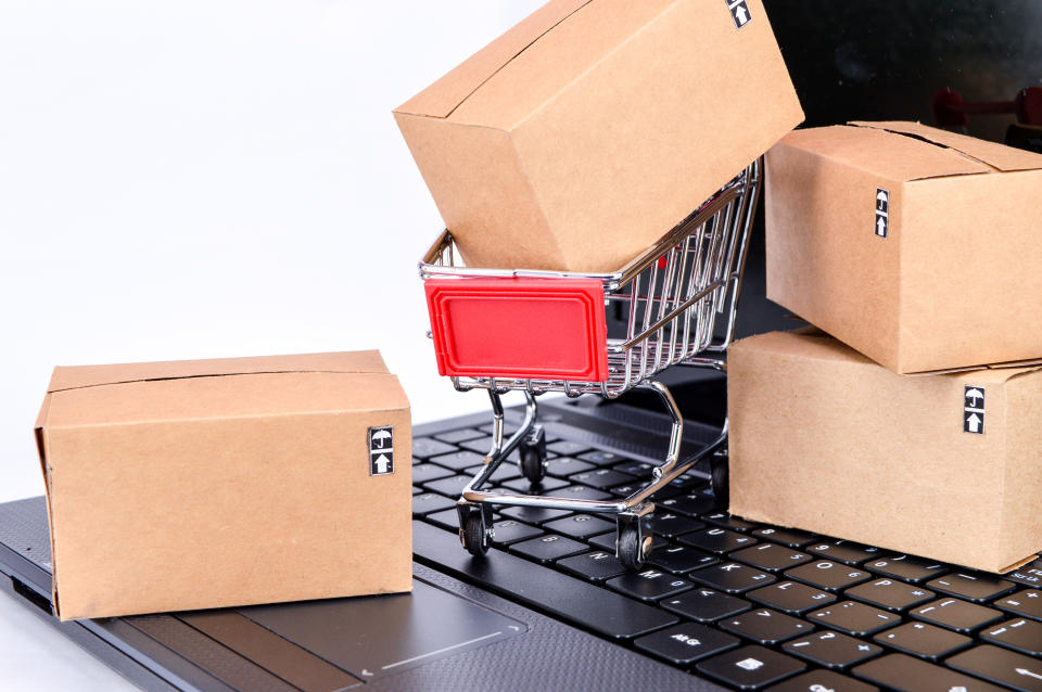 Close-Up Of Small Shopping Cart With Packages On Laptop Over White Background