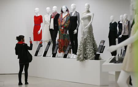 A visitor takes a photo of a display of dresses in the "Women Fashion Power exhibition at the Design Museum in London November 4, 2014. REUTERS/Suzanne Plunkett