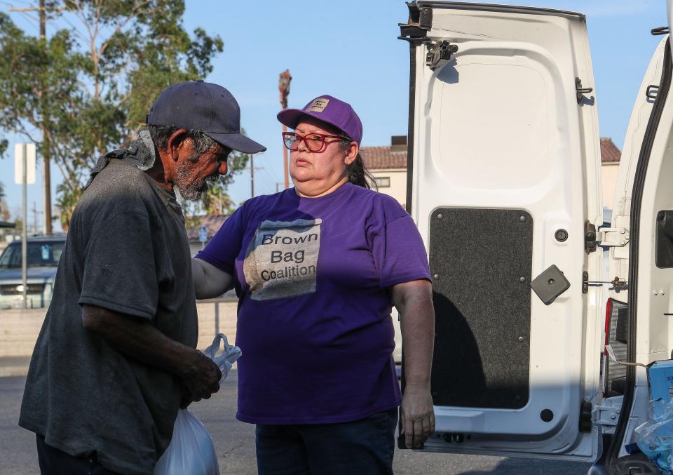 Maribel Padilla places a cold cloth around the neck of Ramon Gonzalez who had been exposed to triple-digit temperatures all day in Calexico, Calif., July 12, 2023.  Padilla is the founder of the Brown Bag Coalition which provides support to unhoused people in Imperial County. 