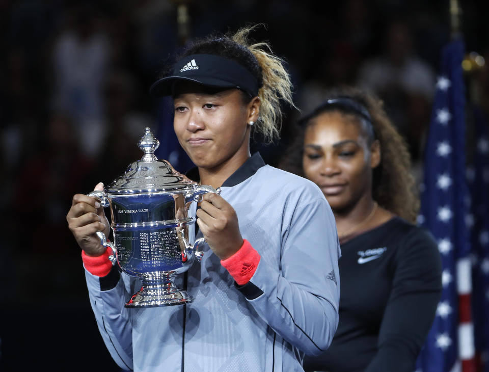 FILE - Naomi Osaka, of Japan, holds the trophy after defeating Serena Williams, rear, in the women's final of the U.S. Open tennis tournament in New York, in this Saturday, Sept. 8, 2018, file photo. Naomi Osaka withdrew from the French Open on Monday, May 31, 2021, and wrote on Twitter that she would be taking a break from competition, a dramatic turn of events for a four-time Grand Slam champion who said she experiences “huge waves of anxiety” before speaking to the media and revealed she has “suffered long bouts of depression.” (AP Photo/Adam Hunger, File)