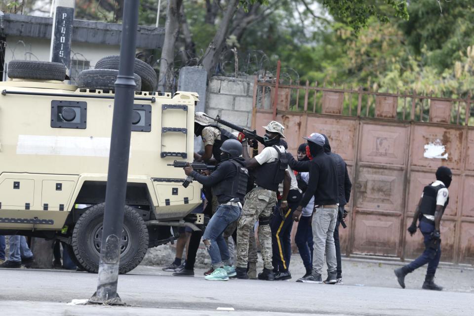 Police officers take cover behind an armored vehicle as they exchange fire with army soldiers during a protest over police pay and working conditions for the national police, in Port-au-Prince, Haiti, Sunday, Feb. 23, 2020. Off-duty police officers and their supporters exchanged fire for nearly two hours with members of the newly reconstituted Haitian army in front of the national palace. (AP Photo/Dieu Nalio Chery)