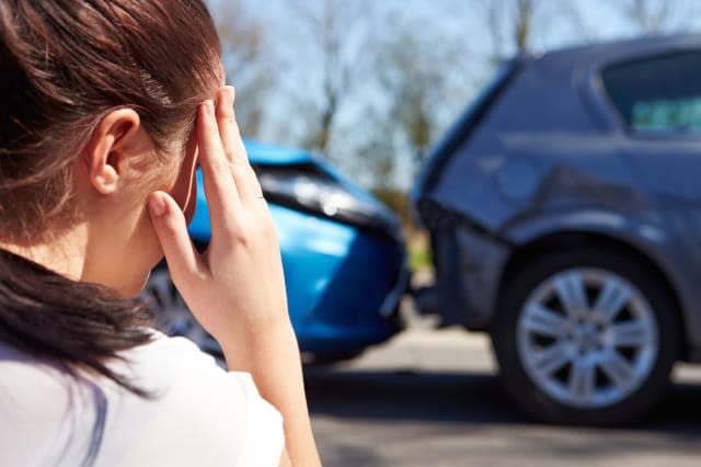 Stressed Driver Sitting At Roadside After Traffic Accident looking at the damage