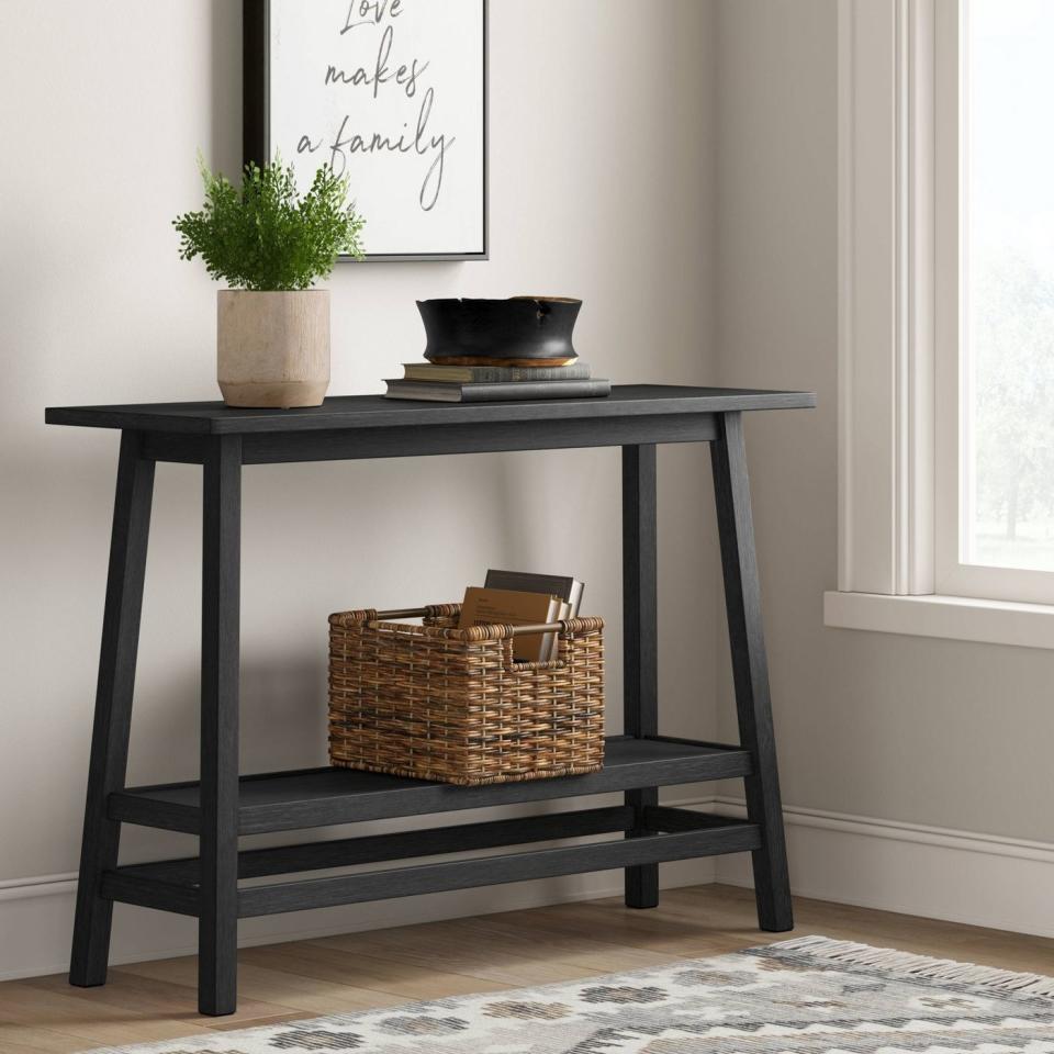 the wood console table in black holding a basket with books and a plant