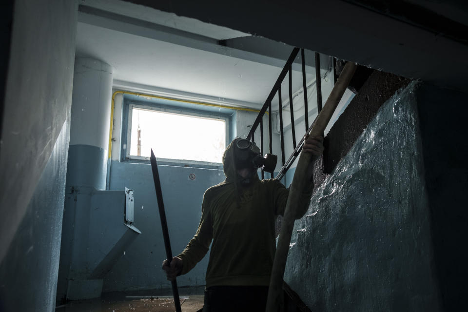 Un hombre con una máscara de gas ayuda a los bomberos a extinguir un incendio en un edificio residencial tras un ataque ruso, en Járkiv, Ucrania, el 21 de abril de 2022. (AP Foto/Felipe Dana)