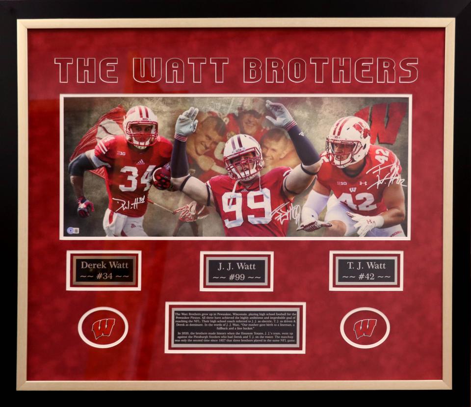 Watt Brothers piece – This framed piece, No. 8 in the International Food Fair oral auction, features the autographs of Watt Brothers – J.J., T.J. and Derek Watt – who are all former Wisconsin Badger football players.