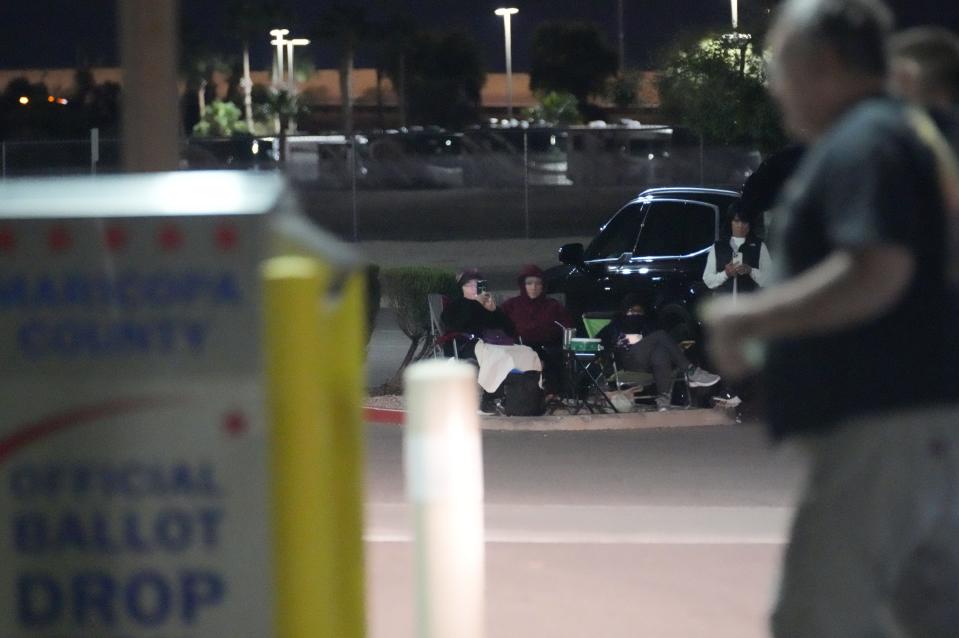 A group of people watches a man deposit a ballot at the Maricopa County early ballot drop box on Oct. 24, 2022, in Mesa.