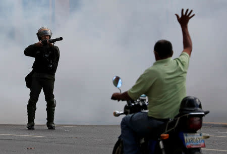 A man on a scooter lifts his hand opposite a security forces officer during a protest of opposition supporters against Venezuelan President Nicolas Maduro's government in Caracas, Venezuela January 23, 2019. REUTERS/Carlos Garcia Rawlins