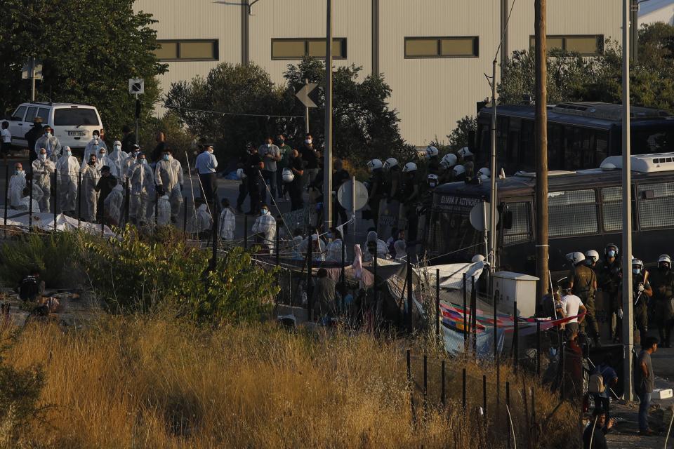 Riot police with buses block the access as their colleagues with special suits to protect against coronavirus, take part in operation to evacuate a road leading from Moria to the capital of Mytilene, where migrants remained camped out on the northeastern island of Lesbos, Greece, Thursday, Sept. 17, 2020. The fires swept through the overcrowded camp at Moria on two nights last week, prompting more than 12,000 migrants and refugees to flee. Most of them remain without shelter even though emergency tents are available at another island site where a new camp is being built. (AP Photo/Petros Giannakouris)