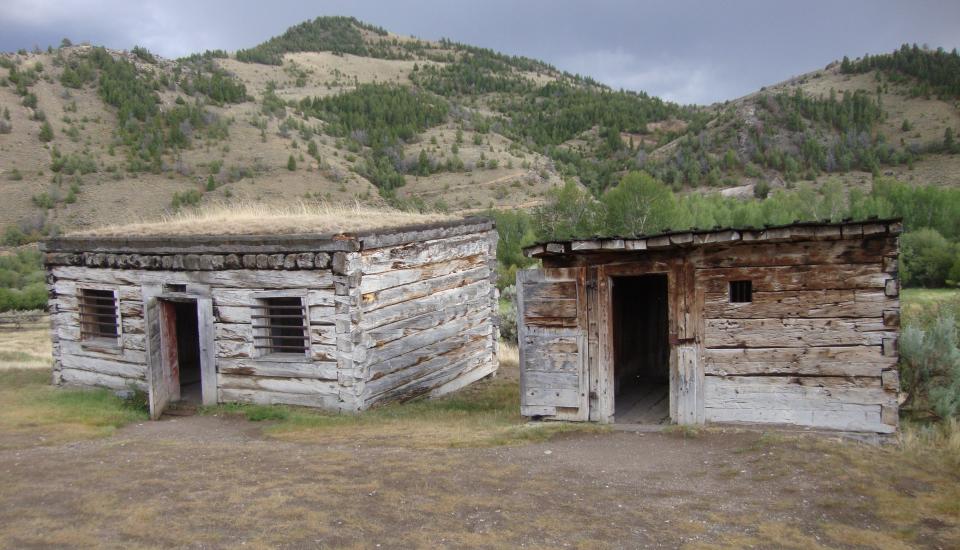 two dilapidated jail cells with hills in the background in Bannack
