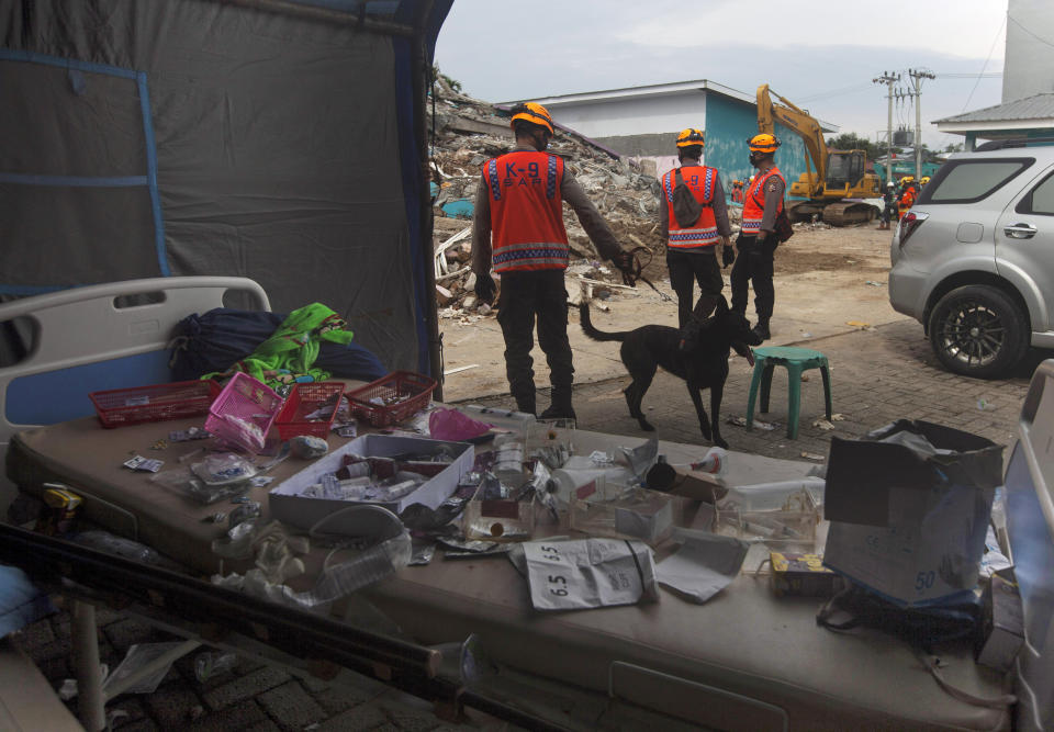 Members of police K-9 squad lead a sniffer dog during a search for victims at a hospital building collapsed in Friday's earthquake in Mamuju, West Sulawesi, Indonesia, Sunday, Jan. 17, 2021. Rescuers retrieved more bodies from the rubble of homes and buildings toppled by the 6.2 magnitude earthquake while military engineers managed to reopen ruptured roads to clear access for relief goods. (AP Photo/Yusuf Wahil)