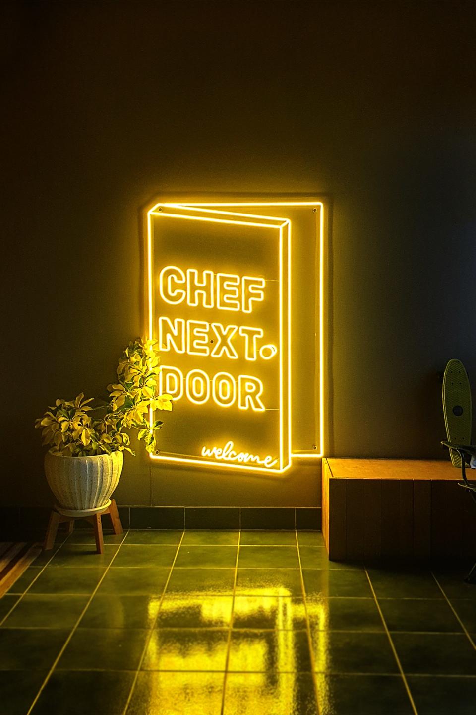 A neon sign greets diners at Chef Next Door