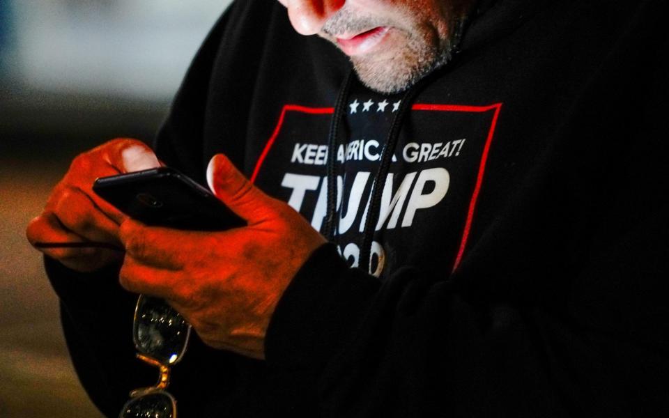 A man wearing a "Trump 2020" sweatshirt uses his mobile phone during a "Stop the Steal" protest outside Milwaukee Central Count the day after Milwaukee County finished counting absentee ballots - BING GUAN/Reuters