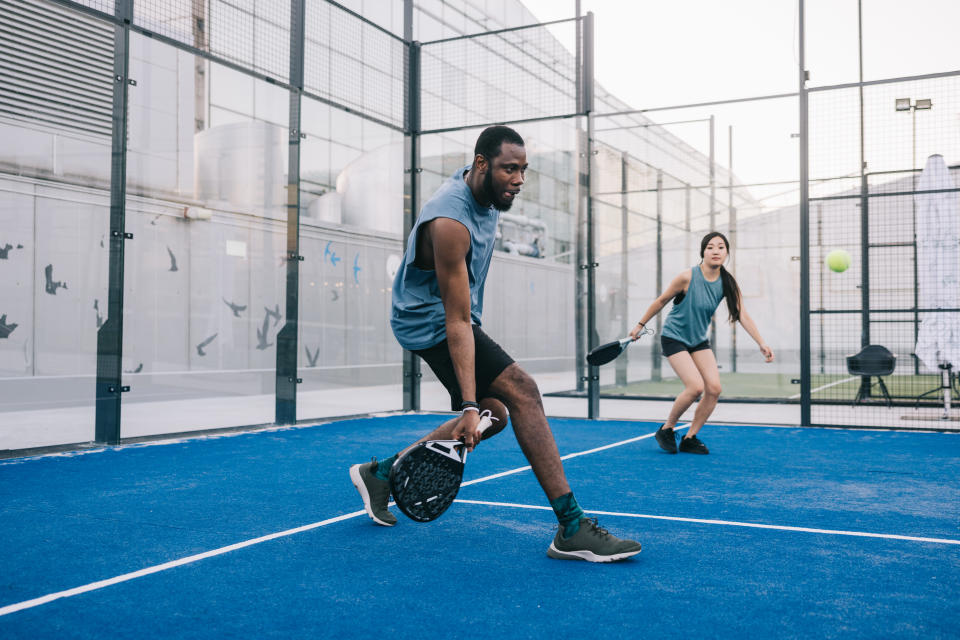 Two positive friends playing paddle tennis on rooftop court