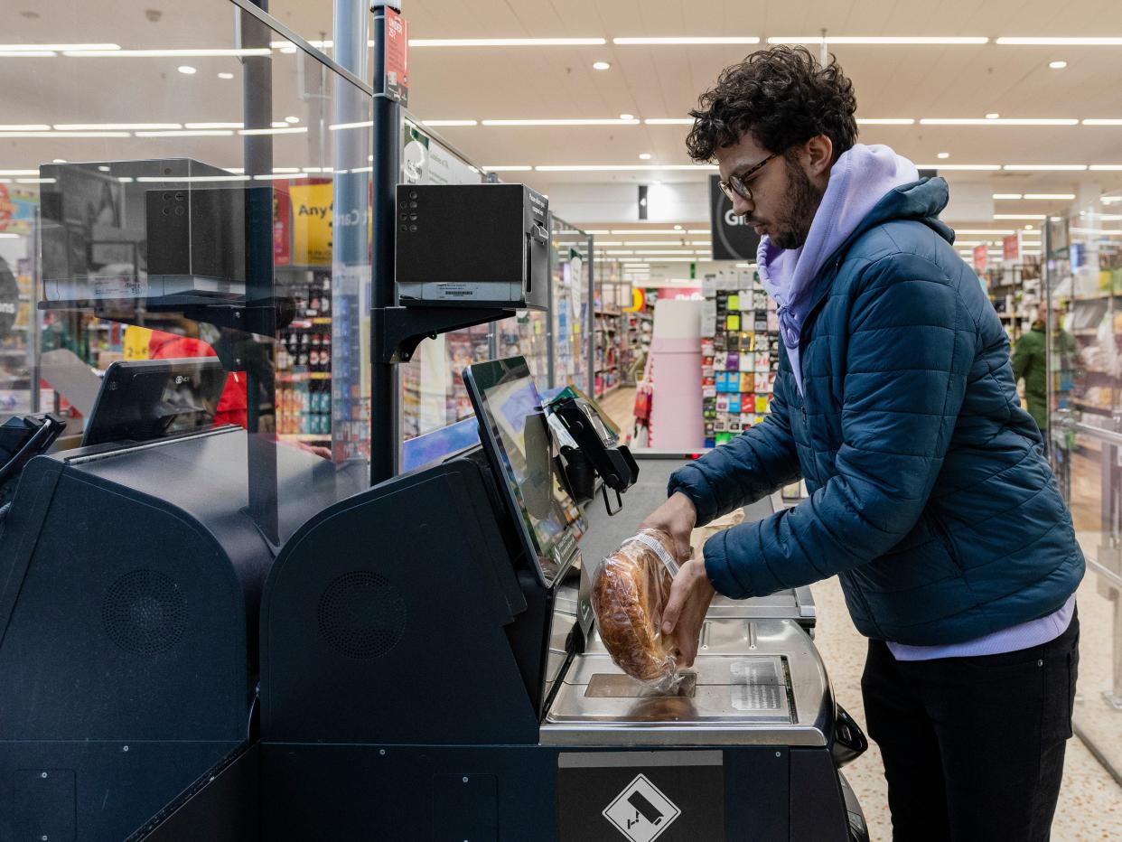 Man scanning a loaf of bread at a self-service kiosk in a store.