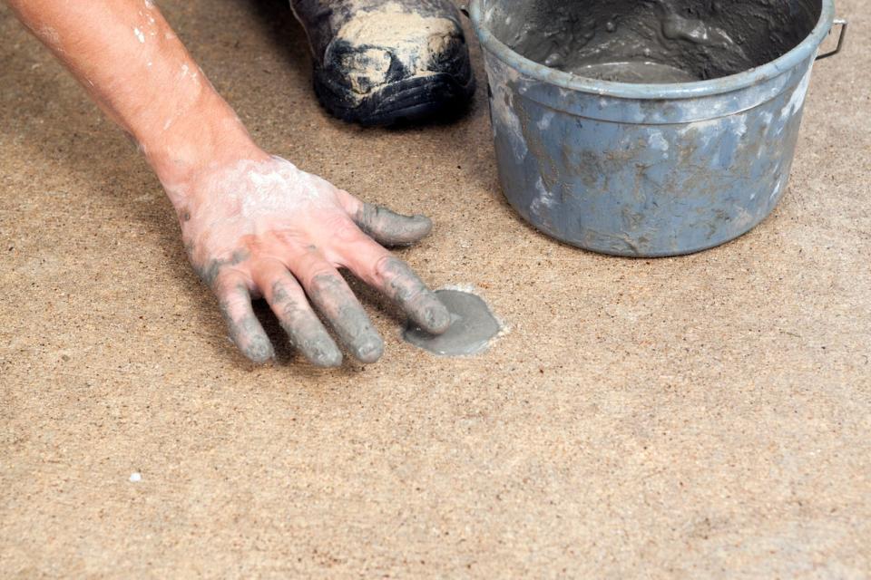 Applying grout to patch a hole drilled in a section of concrete sidewalk 