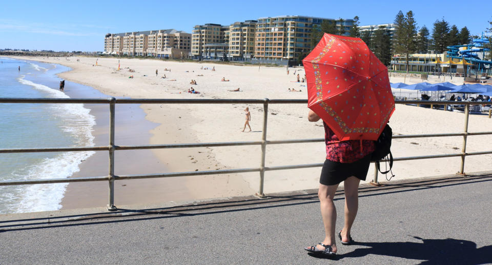 A bystander at Glenlg Beach uses an umbrella for shade. Source: Getty Images