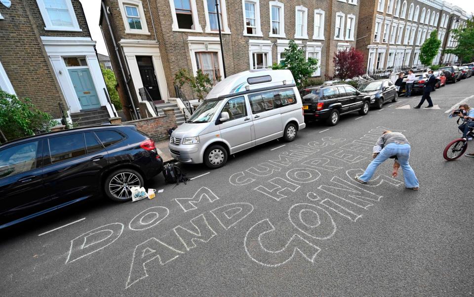 A woman chalks a message onto the road outside the home of Dominic Cummings, reading: 'Dom Cummings and hopefully going' - AFP 