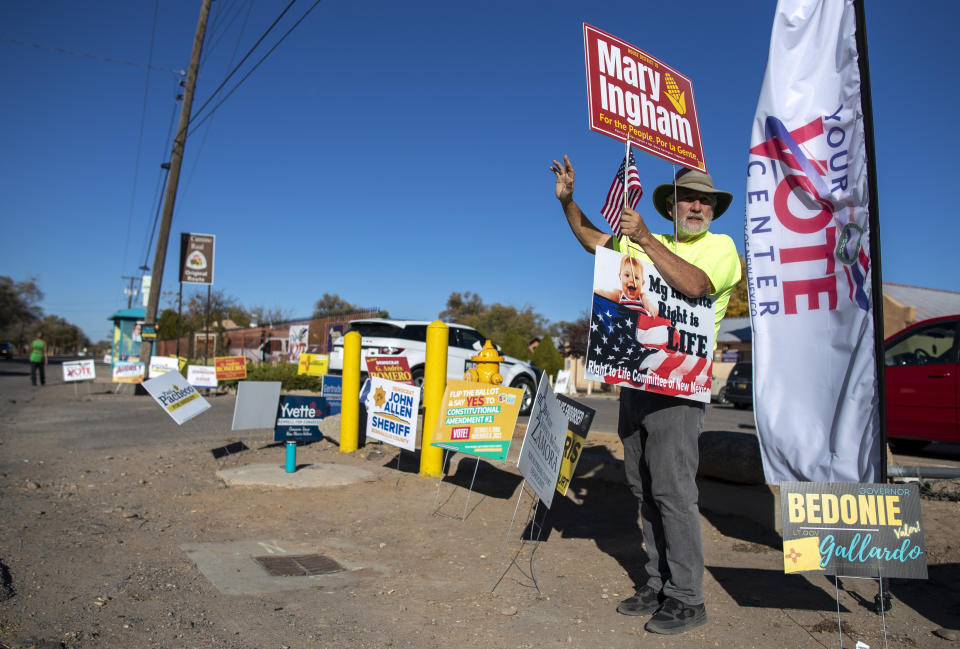 Stewart Ingham waves to motorists while campaigning for his wife Mary Ingham, a candidate for the New Mexico State House of Representatives, outside a polling center in the South Valley area of Albuquerque, N.M., Tuesday, Nov. 8, 2022 (AP Photo/Andres Leighton)