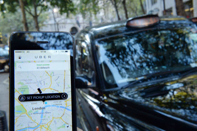 A man holds a smartphone displaying the Uber app as taxis line up on Fleet Street during a protest by the United Cabbies Group (UCG), which represents more than 1,400 London black cab drivers, over the regulation of private hire cars.