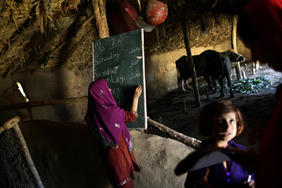 In this Wednesday, March 27, 2013, photo, a Pakistani schoolgirl, center, writes on the blackboard, while her teacher Warda Arshad, 20, right, check the homework of another student during their daily classes in a makeshift school set in a clay house, part of it is used as a cowshed, in a poor neighborhood on the outskirts of Islamabad, Pakistan. Wonder Woman and Supergirl now have a Pakistani counterpart in the pantheon of female superheroes _ one who shows a lot less skin. Meet Burka Avenger: a mild-mannered teacher with secret martial arts skills who uses a flowing black burka to hide her identity as she fights local thugs seeking to shut down the girls' school where she works. Sadly, it's a battle Pakistanis are all too familiar with in the real world.(AP Photo/Muhammed Muheisen)